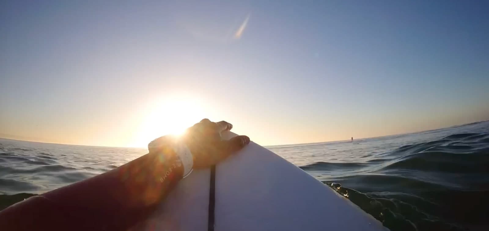 Lever de soleil sur l'océan, la main posée sur la planche de surf